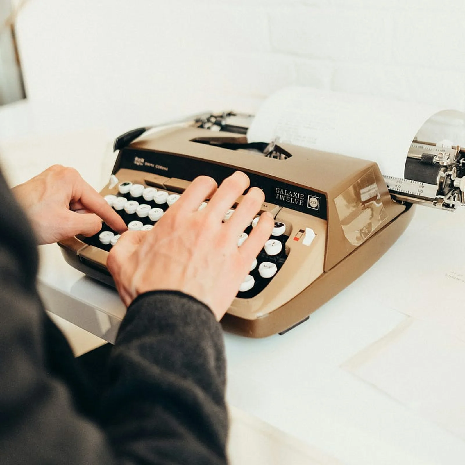A person typing on a beige vintage Galaxie Twelve typewriter, with a sheet of paper fed into the machine.